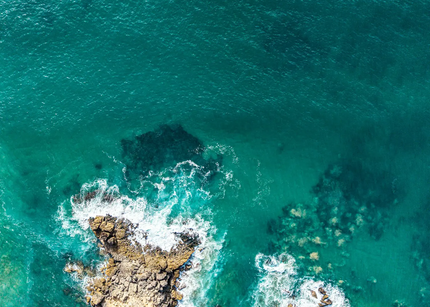 Turquoise water breaking over rocks seen from above
